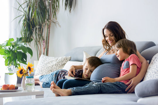 Young pregnant woman, reading a book at home to her two boys