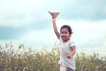 Cute asian child playing toy paper airplane in the meadow in vintage color tone