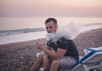 Man with beard smoking electronic sigarette on sunset beach