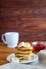 Pancakes with bananas and hot tea on a wooden background. Dietary breakfast