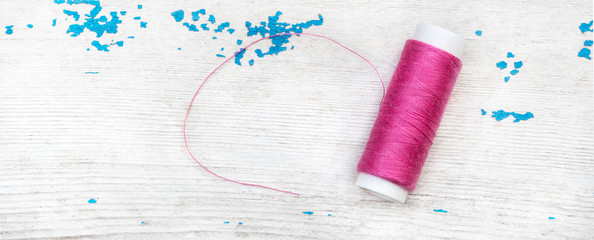 Spool of pink thread on the wooden background.