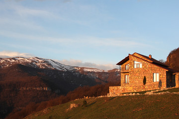 Fototapeta na wymiar lonely stone house on the hill on the background of snowy mountains, at sunrise, horizontal