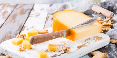 Delicious dutch gouda cheese with cheese blocks, crackers, walnuts and special knife on old wooden table. - obrazy, fototapety, plakaty