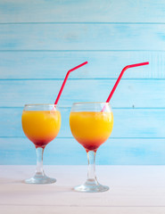Two cocktails with orange juice and tequila on a blue background. Summer drink with a straw in a glass