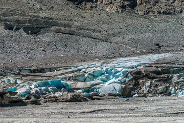 Gletschereis schimmert blau unter dem Überzug aus Steinen und Sand