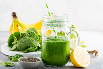 Healthy green smoothie with spinach, banana, lemon, apple and chia seeds in glass jar and ingredients. Detox, diet, healthy, vegetarian food concept.
