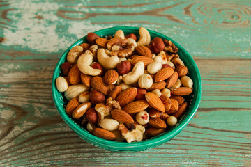 Mixed nuts in a turquoise bowl on a turquoise and white wooden background.