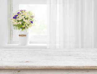 Fototapeta na wymiar Rustic table in front of wild flowers on wooden window