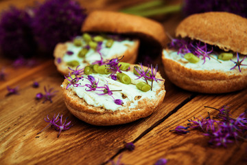 Toasted bread bruschetta with cream cheese and garlic edible flowers on olive wooden cutting board on stone slate gray background. Top view