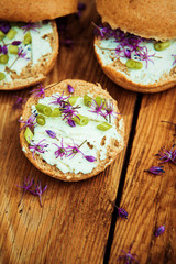 Toasted bread bruschetta with cream cheese and garlic edible flowers on olive wooden cutting board on stone slate gray background. Top view