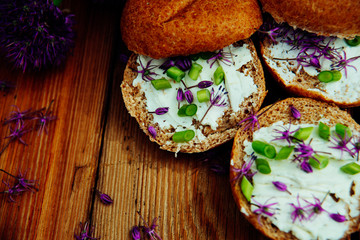 Toasted bread bruschetta with cream cheese and garlic edible flowers on olive wooden cutting board on stone slate gray background. Top view