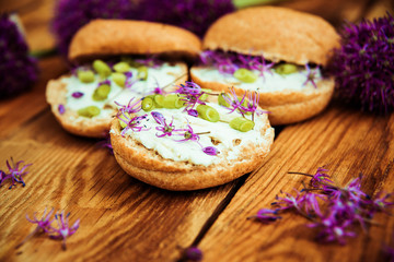 Toasted bread bruschetta with cream cheese and garlic edible flowers on olive wooden cutting board on stone slate gray background. Top view