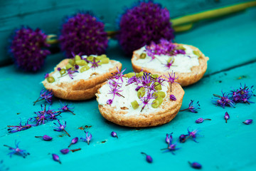Toasted bread bruschetta with cream cheese and garlic edible flowers on olive wooden cutting board on stone slate gray background. Top view