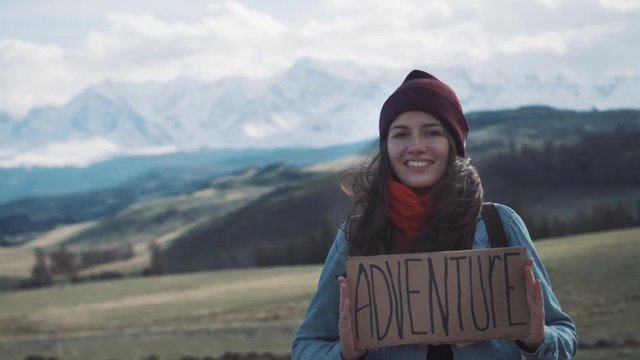 Teenage Girl Holding An Adventure Sign On A Mountain Road, Smiles And Laughs.