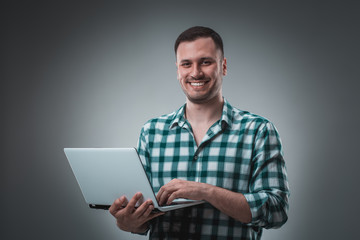 Attractive business man model in green shirt isolated on gray working with laptop, showing something by left hand.