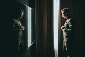 Stylish groom in gray suit posing near window