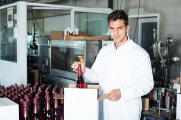smiling male employee in coat packing bottles into carton package