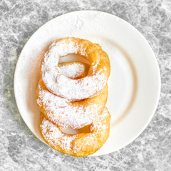 Fresh donuts topped with white sugar powder on a plate on colorful background close up. Russian traditional donuts