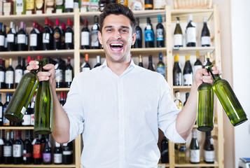 Cheerful man holding wine bottles in winery section