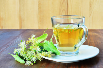 Linden tea in glass mug with linden flowers on wooden table
