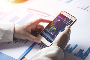 Handle the phone to check the stock with Sunset light background.