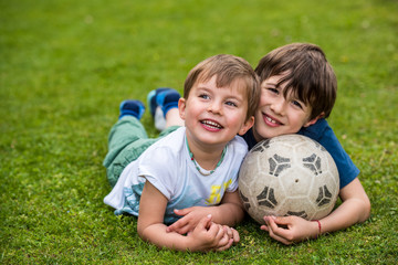 Fototapeta premium Two kids laying on the grass with a soccer ball