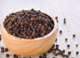 Black peppercorns on white wooden background
