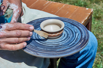 On the potter's wheel revolve a spinning of a clay cup. The potter with a wooden stick forms a picture on the cup