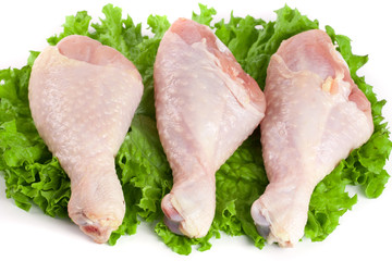 Three raw chicken drumsticks with lettuce leaf isolated on white background