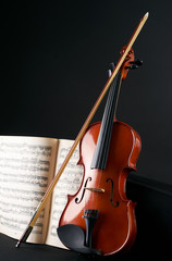 Close-up photo of vintage violin with bow and musical notes. Cello or fiddle and fiddlestick on ancient music sheet, rusted old yellow paper, sheet of music on black background.