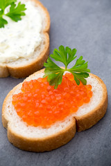 Bread with fresh cream cheese and red caviar on table.