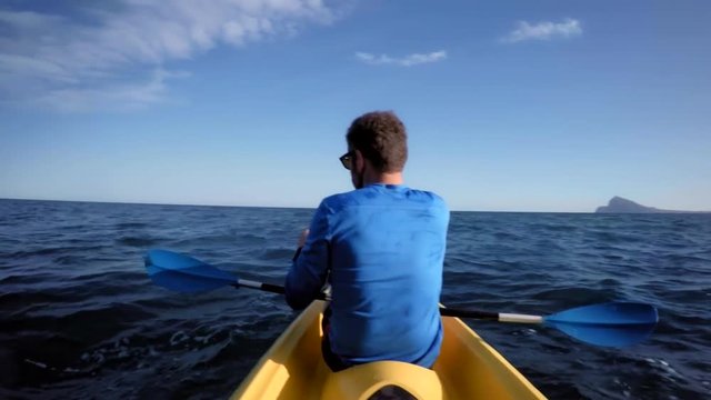 Action camera footage of athletic sporty man with healthy lifestyle choices paddles yellow kayak through open ocean waters with waves, stops to take breath, rest and drink refreshment from flask