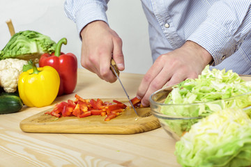 Hands of man chopped red bell pepper for salad on board, close-up
