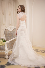 Fototapeta premium the girl is back in a wedding dress next to a vintage chair in bright room