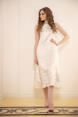 the girl  in a white evening dress looking to the side in front of a white wall