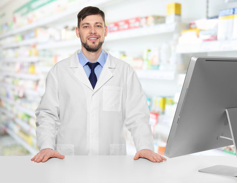 Young handsome pharmacist standing at table on white background