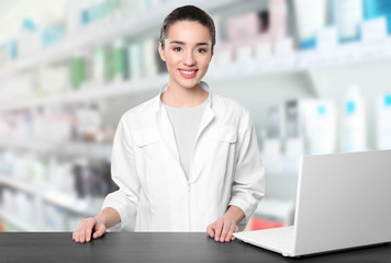 Young woman pharmacist standing at table on grey background