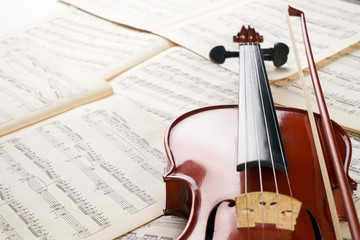 Fototapeta premium Close-up photo of vintage violin with bow and musical notes. Cello or fiddle and fiddlestick on ancient music sheet, rusted old yellow paper, sheet of music.