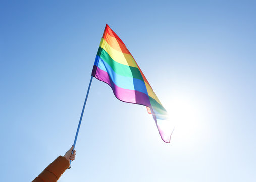 Woman holding gay flag on blue sky background. Concept of sexual minority