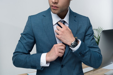 Cropped shot of stylish young businessman in suit adjusting tie in office