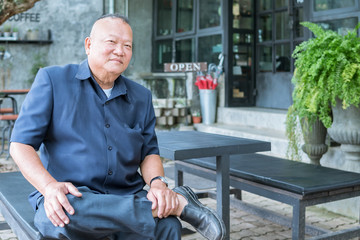 Portrait of asian senior Smiling man and he sit with one's legs crossed on front of coffee shop background.