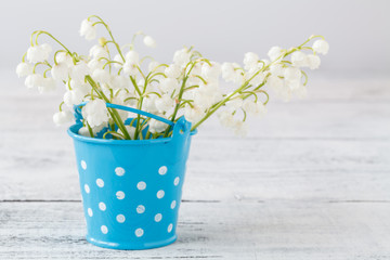 Lily of the valley bouquet in vase on a white wooden background