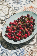 Fresh ripe sweet cherries in blue plate over colorful oriental ceramic tiles background, selective focus. Summer food concept
