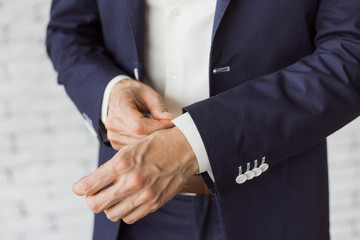 Obraz premium Closeup of elegant young fashion man dressing up for wedding celebration. Color close up image of male hands. Handsome groom dressed in modern blue formal suit, white shirt getting ready for event.