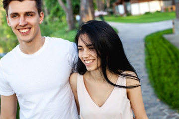 The guy hugs the waist of the girl with a shy smile while walking in nature. Beautiful young couple during a romantic date.