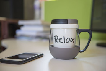 Cup “relax” on the white table  and phone in the office .
