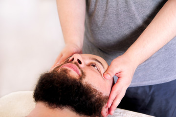 Fototapeta na wymiar Man having treatment for his face at massage table, medicine concept. Masseur massaging mans face. Handsome man relaxing receiving facial massage at spa center relaxation therapy resort recreation.