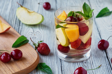 Fresh fruit detox water in a glass cup. Apple, cherry, peach, strawberry wooden table.