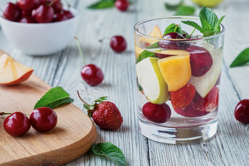 Fresh fruit detox water in a glass cup. Apple, cherry, peach, strawberry wooden table.