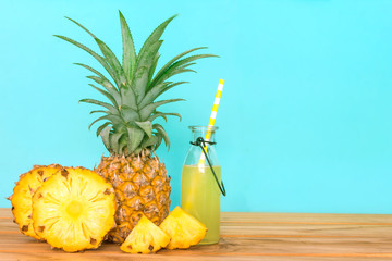 The Bottles of pineapple juice with sliced pineapple fruit on wooden table with fresh blue...